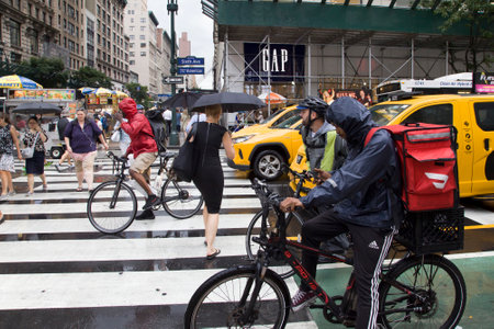 NEW YORK, NEW YORK/USA - July 22, 2019: Bikers and autos wait at 6th avenue corner as pedestrains cross street.のeditorial素材
