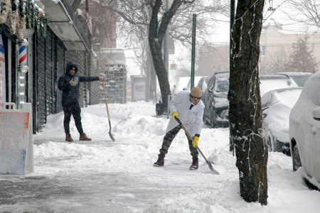 BRONX, NEW YORK, USA - January 29, 2022: Hispanic men shovel snow in front of barber business during snow storm.のeditorial素材