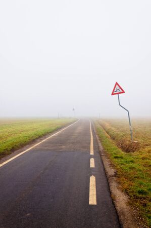 Foggy empty rural road with danger signの写真素材