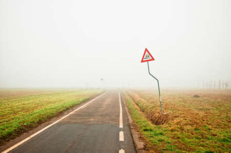 Foggy empty rural road with danger signの写真素材