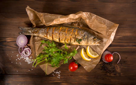 healthy food: two fried sea bass fish served with tomatoes and vegetables on big wooden board over tableの写真素材