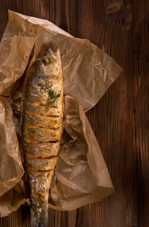 healthy food: two fried sea bass fish served with tomatoes and vegetables on big wooden board over tableの写真素材