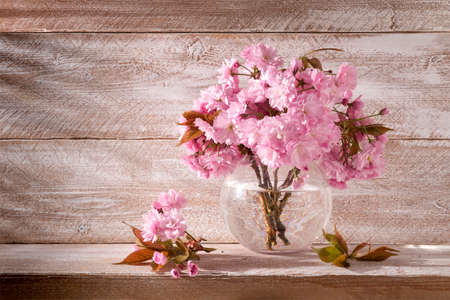 Sakura flowers in a round vase on a wooden background still life beautiful gentle pink colorの写真素材