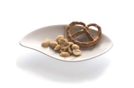 Peanuts and pretzel on white porcelain bowl, isolated on whiteの写真素材