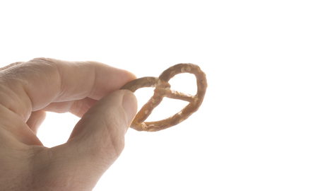 Fingers hold a salt pretzel, isolated on white backgroundの写真素材
