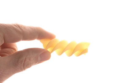 Two fingers hold a spiral noodle (fusilioni), isolated on whiteの写真素材