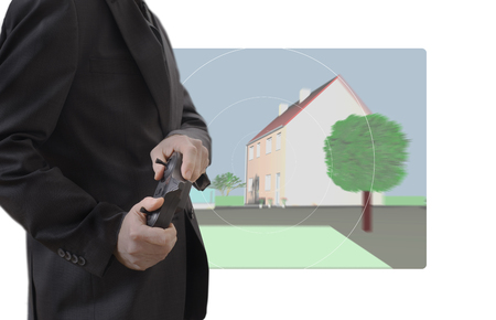 A man holds a remote control in his hands, in the background a screen with a residential complex (3D design)の写真素材