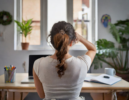 Rear view of businesswoman scratching her head while sitting at desk in officeの素材