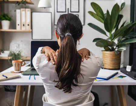 back view of businesswoman sitting at desk and touching hair in officeの素材