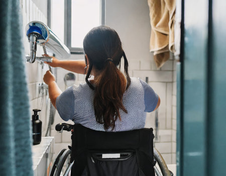 Young woman in wheelchair washing her hands in the bathroom at home.の素材