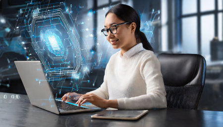 Businesswoman working on laptop in modern office with glowing padlock hologramの素材