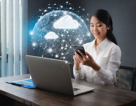 Businesswoman using mobile phone and laptop with cloud computing icon on screen.の素材