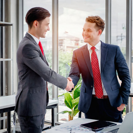 Image of two young businessmen shaking hands in office. Business meeting conceptの素材