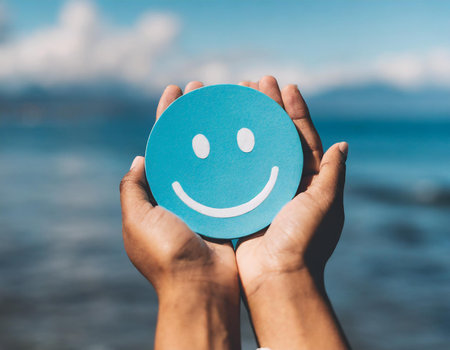 hand holding a blue smiley face on the beach with ocean backgroundの素材