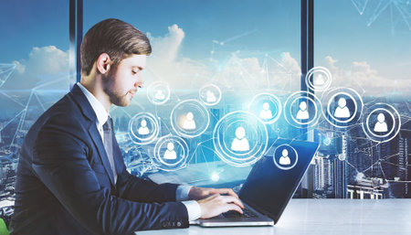 Side view of young businessman using laptop with double exposure of social network interface. Toned imageの素材