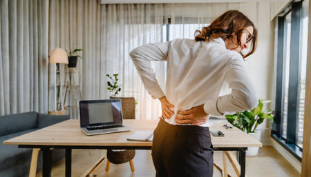 Businesswoman suffering from back pain while working in office. Backache conceptの素材