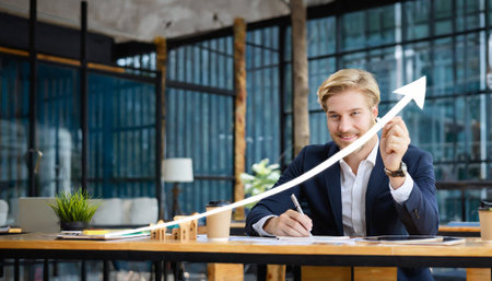 Portrait of confident businessman writing on paper while sitting at table in officeの素材