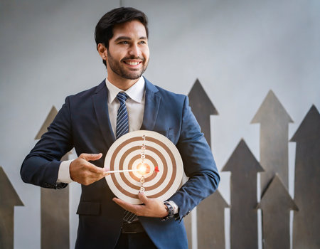 Portrait of a smiling young businessman holding a target with arrows pointing upの素材