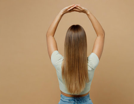 Back view of young woman with long blonde hair on beige backgroundの素材