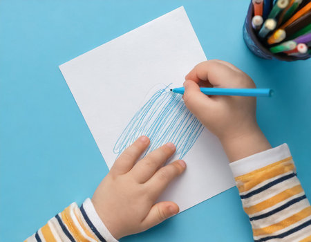 Child draws with felt-tip pens on a white sheet of paperの素材