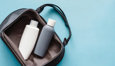 Set of cosmetic bottles in a black bag on a blue background.の素材