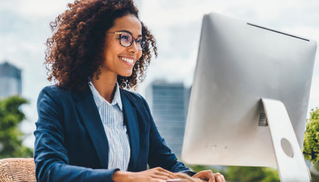 Portrait of smiling young businesswoman working on computer while sitting outdoors.の素材