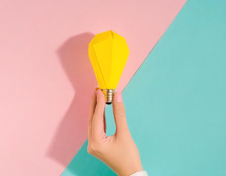 Female hand holding yellow lightbulb on a blue and pink backgroundの素材