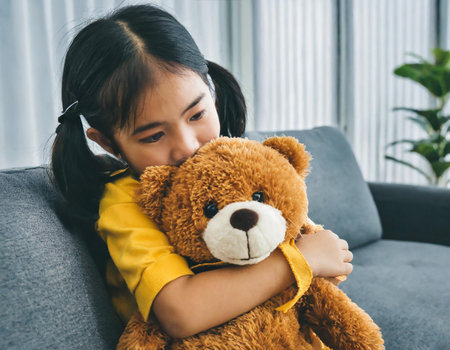 Little asian child girl hugging teddy bear on sofa at homeの素材
