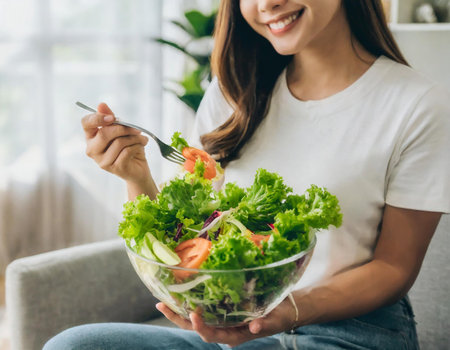 Cropped image of young asian woman eating fresh salad at homeの素材