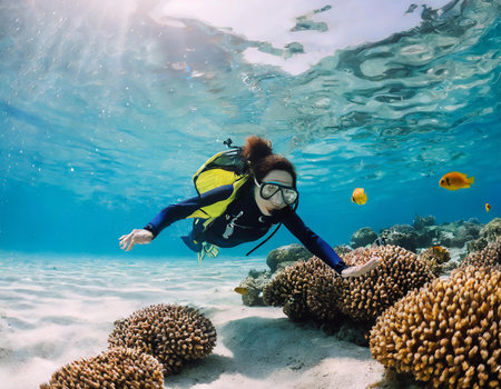 Underwater view of a young woman scuba diver swimming over coral reefの素材