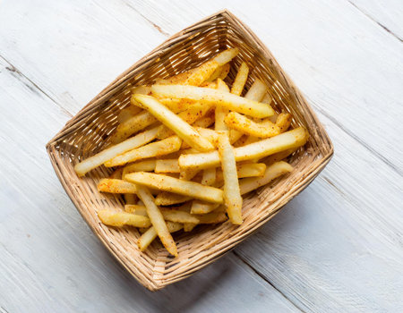Golden French fries in a basket on white wooden background. Top view.の素材