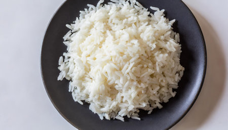 Cooked white rice in a black plate on a white background.の素材