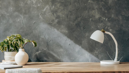 Ceramic vase with plant and lamp on wooden table near grey wallの素材