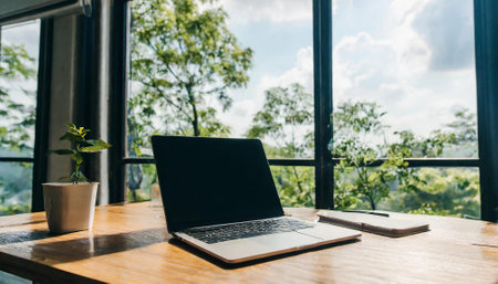 Laptop computer on wood table in coffee shop with nature view backgroundの素材