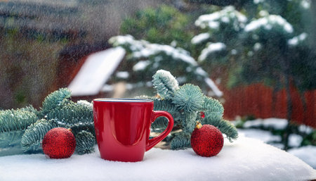 red mug and christmas decorations in the courtyard of the house on a snowy winter dayの素材