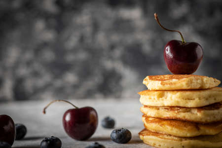 Stacked hot cakes with cherries strawberries and blueberries on a vintage black wooden table. Space...