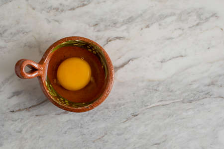 yolk and egg white in an earthenware container, on a gray marble bar.