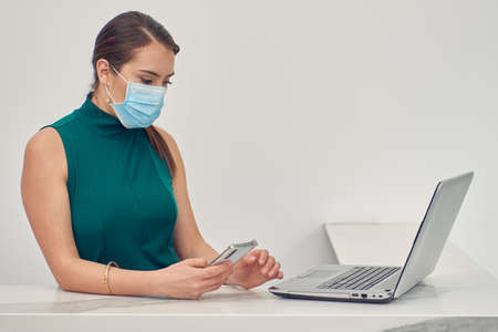 Executive woman checking and answering messages on her cell phone, wearing a mask due to normality due to the covid-19 pandemicの写真素材