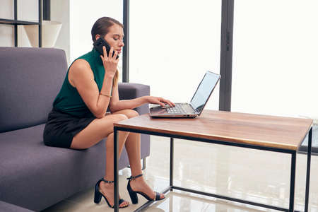 Executive woman at home, answering call and working on her laptop, from her living room.の写真素材