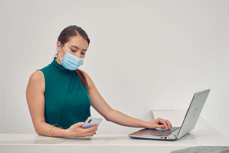 Executive woman checking emails on computer, wearing mask due to the new normal due to the covid-19 pandemicの写真素材