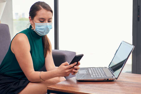 Woman with mouthpiece answering messages on cell phone from home due to the new normal due to the covid-19 pandemicの写真素材