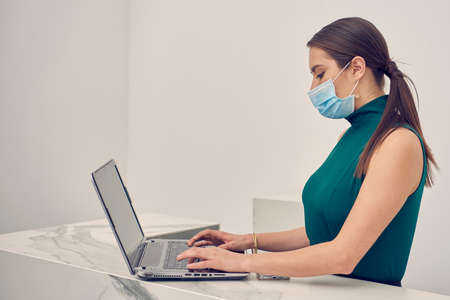 Executive woman checking emails on computer, wearing mask due to the new normal due to the covid-19 pandemicの写真素材