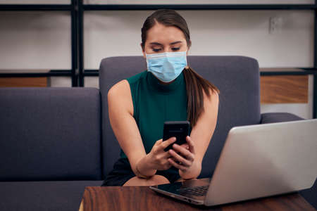 Woman with mouthpiece answering messages on cell phone from home due to the new normal due to the covid-19 pandemicの写真素材