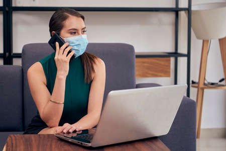 Woman with mouth cover working at home due to the new normal due to the covid-19 pandemicの写真素材
