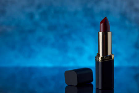 Deep burgundy lipstick on a marble surface with a blue background and space for text on the left