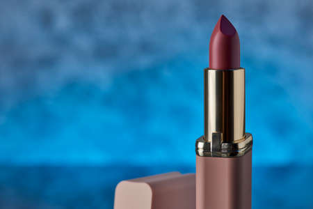 Pink lipstick on a marble surface with a blue background and space for text on the left side