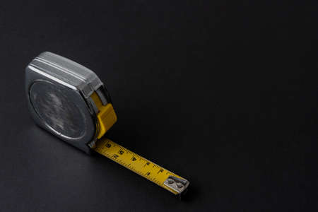 Silver color flexometer or meter with yellow tape measure on a black background