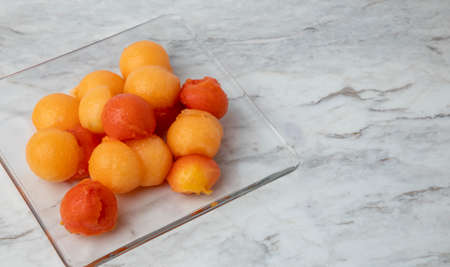 Fruit balls in a glass dish, on a white marble bar with a spoon and cutterの写真素材