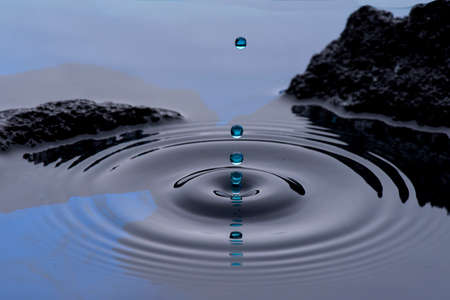 Drops of blue water frozen in the air and forming waves on the liquid surface, with rocks or stones...