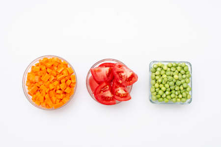 Carrot, tomato and pea to make red rice in glass containers with white backgroundの写真素材